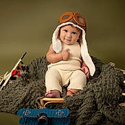 Maximiliano joined the competition — help win amazing prizes! baby, child, pilot_hat, knitwear, toy_airplanes, blanket, smile, thumbs_up, portrait, indoor, cute, infant, vintage_style, playful, cozy, seat, headwear, footwear, red_bracelet, studio