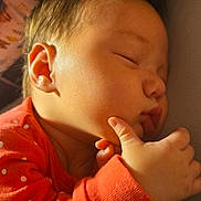 Lila is registered to the contest to win money with this photo: baby, sleeping, infant, orange_clothing, polka_dot, hand, thumb, face, cheek, peaceful, close_up, portrait, skin, cute, child, newborn, rest, cozy, indoors, soft_light