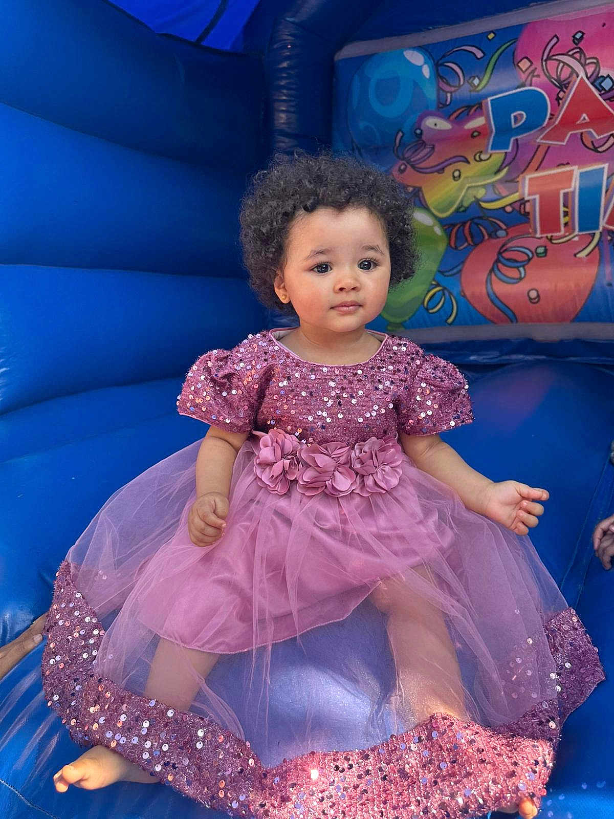 Alyza joined the competition — help win amazing prizes! toddler, child, curly_hair, pink_dress, sequin, inflatable, bounce_house, blue, sitting, barefoot, flower_belt, indoor, portrait, cute, young_child, play_area, colorful, fun, event, party
