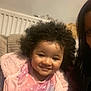 Alyza joined the competition — help win amazing prizes! child, toddler, curly_hair, smiling, pink_jacket, plush_clothing, indoor, sofa, cushion, radiator, portrait, happy, close_up, face, skin, black_hair, hair, cozy, person, adult_partial