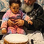 child, toddler, grandparent, elderly_man, beard, cake, layered_cake, dessert, table, pajamas, holding, sitting, indoor, wallpaper, hands, knife, plate, family, portrait, food