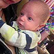 Kody is registered to the contest to win money with this photo: baby, infant, person, face, closeup, holding, adult, indoor, holiday_lights, christmas_tree, couch, clothing, striped_shirt, expression, curious, skin, head, eyes, nose, mouth