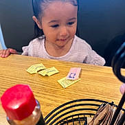 Marisol joined the competition — help win amazing prizes! child, girl, pigtails, table, wood, sweetener_packets, condiment, bottle, red_cap, black_holder, indoor, curious, young, person, casual, dining, food_related, seat, restaurant, focus_blur