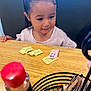 child, girl, pigtails, table, wood, sweetener_packets, condiment, bottle, red_cap, black_holder, indoor, curious, young, person, casual, dining, food_related, seat, restaurant, focus_blur
