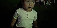 Marisol is registered to the contest to win money with this photo: child, night, outdoor, grass, people, lights, curious, white_shirt, dark, blurred, gathering, event, lawn, casual, portrait, face, person, young, evening, crowd