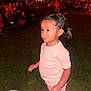 child, toddler, pajamas, grass, nighttime, outdoor, crowd, people, bracelet, hair_tied, light, event, audience, young_child, curious, standing, person, face, expression, casual_clothing