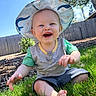 baby, child, smiling, hat, sunhat, grass, outdoor, blue_sky, fence, tree, greenery, happy, sitting, casual_clothing, shorts, toddler, daylight, nature, portrait, playful