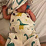 baby, infant, pacifier, hat, clothing, dinosaur_print, sleeping, bed, blanket, cute, newborn, child, soft, resting, comfort, fabric, pattern, small, peaceful, skin