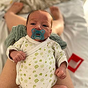 Bruno participe au concours pour gagner de l'argent avec cette photo : baby, pacifier, onesie, infant, legs, hand, face, person, patterned_clothing, blurred_background, skin, newborn, indoor, resting, cute, small, fist, comfort, soft, lying