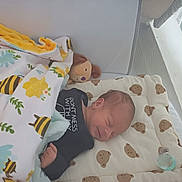 Milo a rejoint le concours — aidez-le/la à gagner de superbes lots ! baby, newborn, sleeping, crib, blanket, teddy_bear, plush_toy, pacifier, bedroom, infant, cute, cozy, child, soft, pattern, fabric, resting, peaceful, indoors, clothing