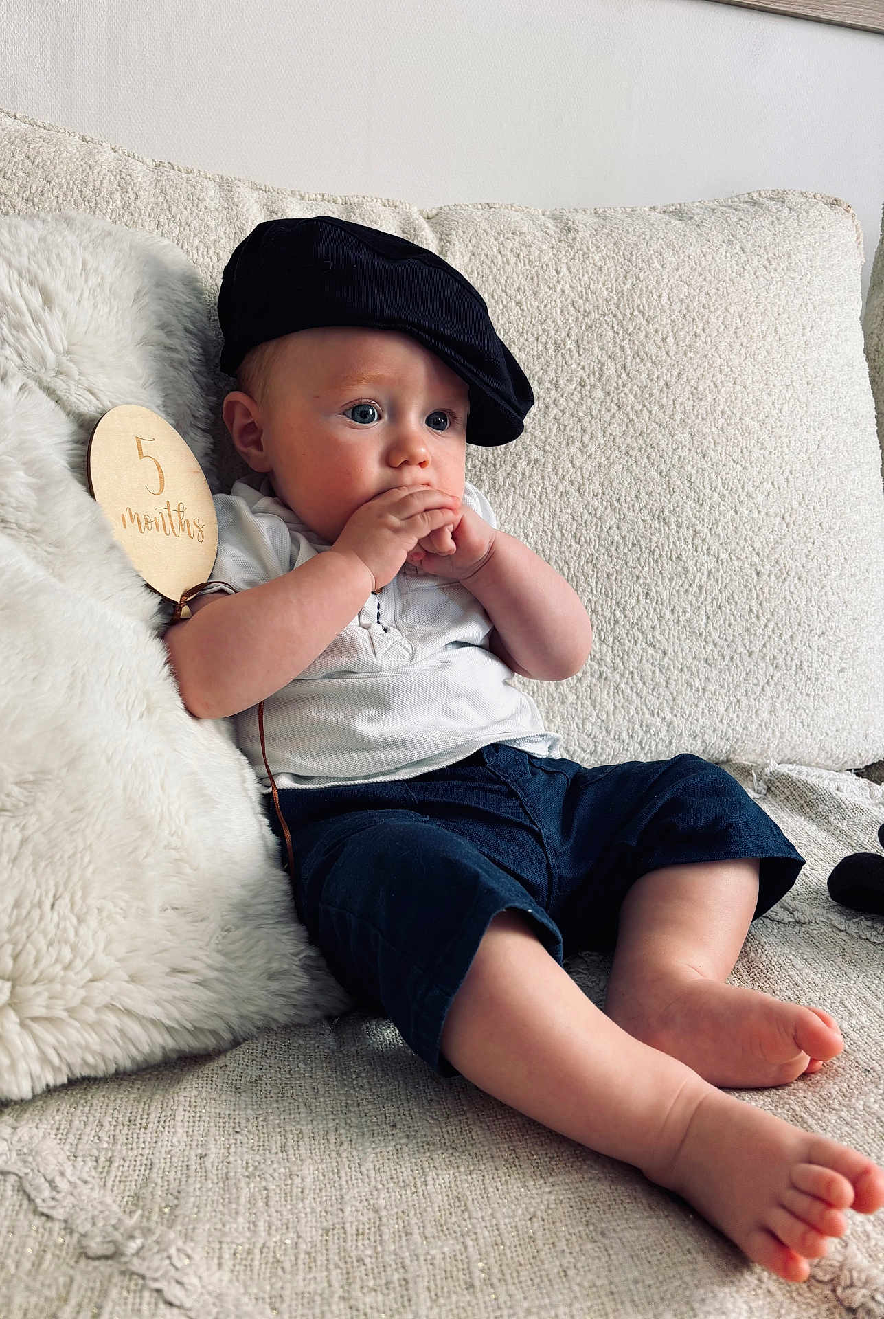 Lowen a rejoint le concours — aidez-le/la à gagner de superbes lots ! baby, infant, child, cap, hat, couch, pillow, white, blue_eyes, clothing, hands, feet, wooden_sign, milestone, sitting, curious, indoors, texture, home, portrait