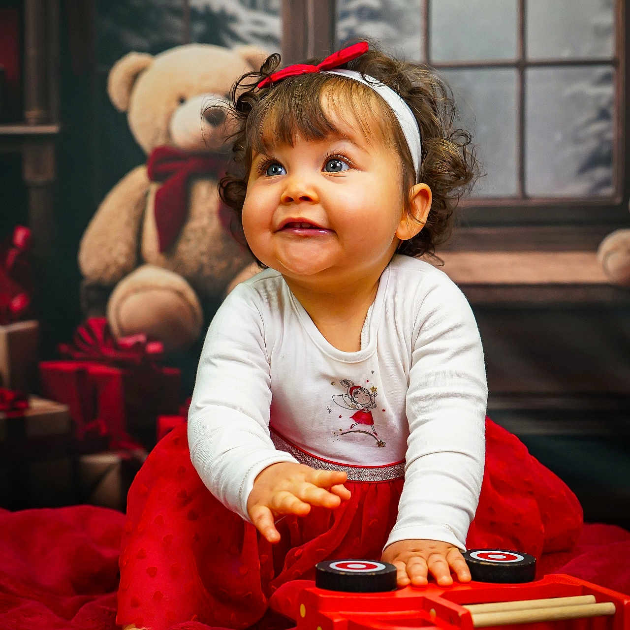 Mya participe au concours pour gagner de l'argent avec cette photo : blanket, child, curly_hair, festive, floor, gift_boxes, happy, holiday, indoor, playful, portrait, red_bow, red_skirt, smiling, teddy_bear, toddler, toy, white_shirt, window, wooden_toy