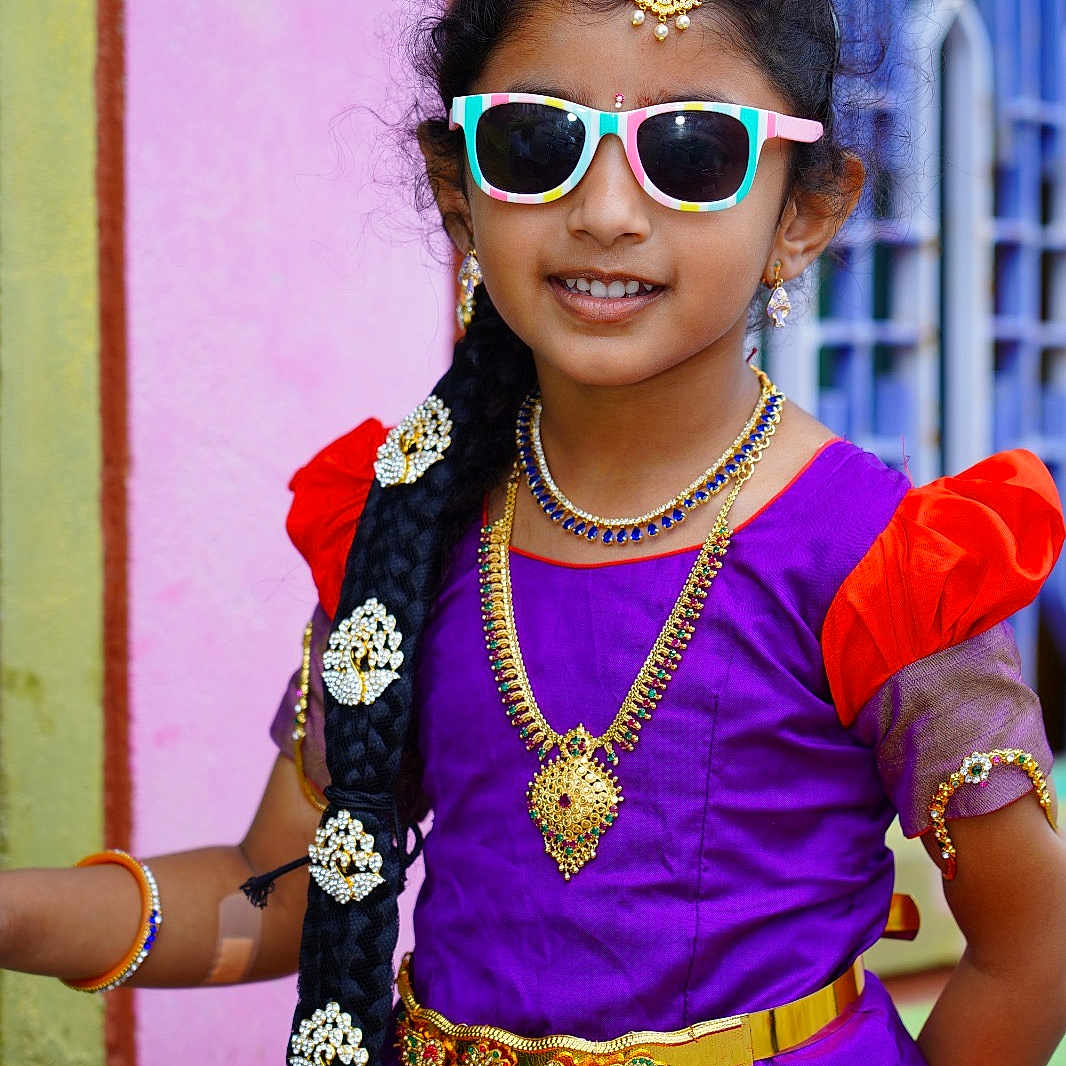 Dhruvishaa Reddy is registered to the contest to win money with this photo: accessories, bodypart, child, clothing, dress, eveningdress, face, female, finger, formalwear, girl, hand, happy, head, jewelry, necklace, person, purple, smile, sunglasses