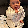 baby, child, infant, smiling, happy, portrait, sitting, couch, blanket, pajamas, clothing, curly_hair, dark_background, indoor, home, face, eyes, open_mouth, cozy, photography