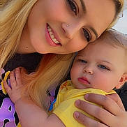 Serenity is registered to the contest to win money with this photo: woman, baby, child, blonde_hair, smile, outdoor, yellow_clothing, holding, portrait, face, family, happy, together, skin, person, hand, casual, daylight, closeup, mother