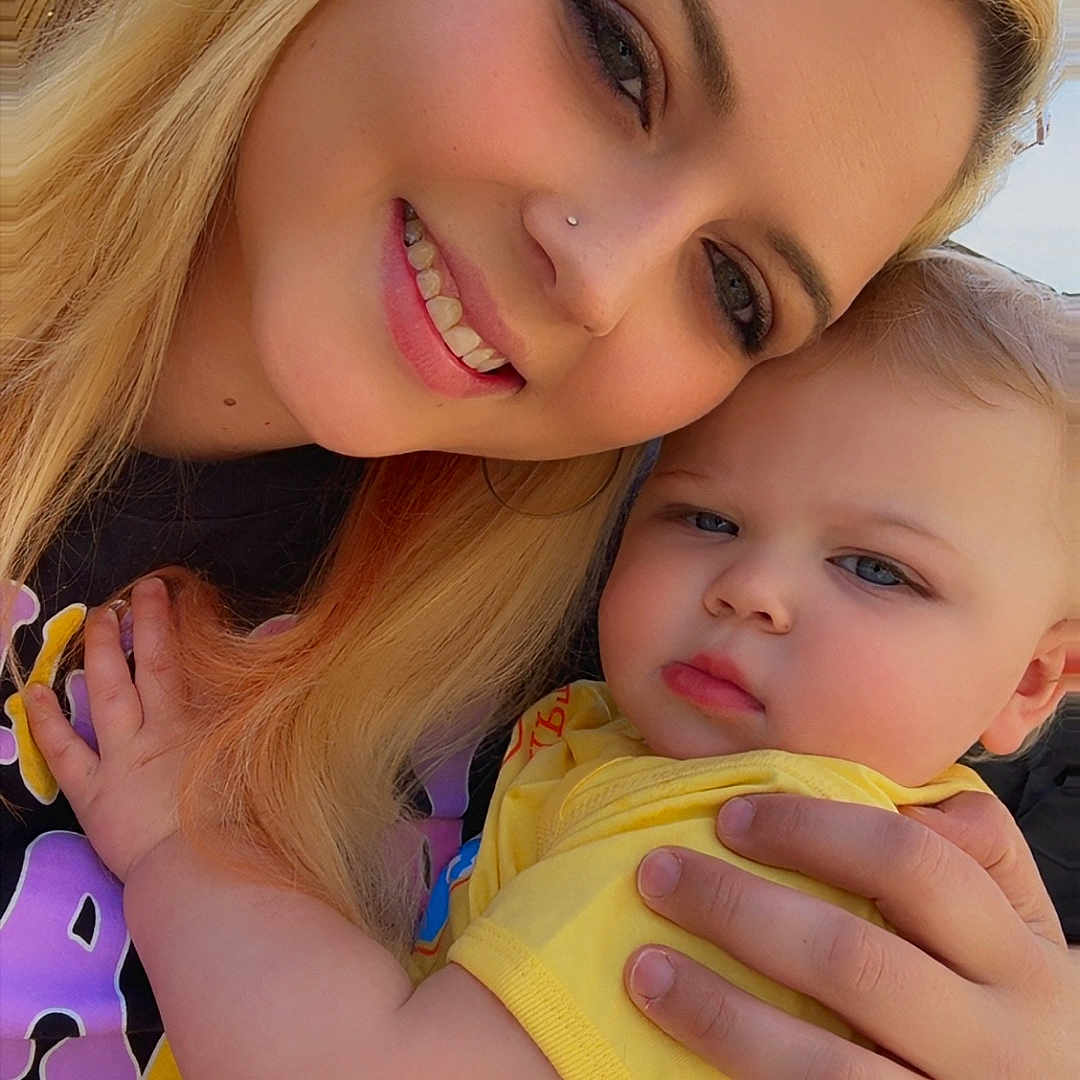 Serenity is registered to the contest to win money with this photo: woman, baby, child, blonde_hair, smile, outdoor, yellow_clothing, holding, portrait, face, family, happy, together, skin, person, hand, casual, daylight, closeup, mother