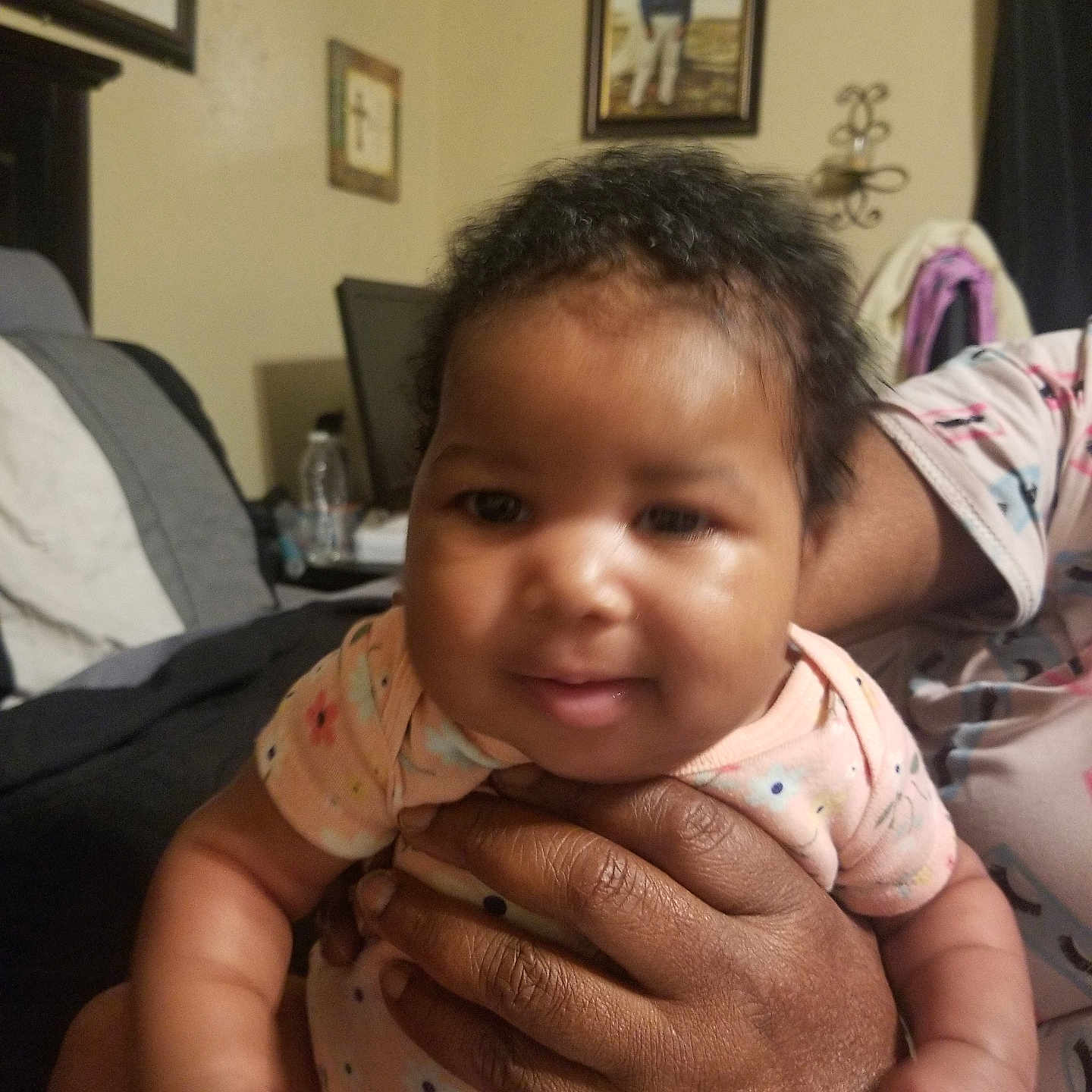 De'Nai joined the competition — help win amazing prizes! adult_hand, baby, bed, child, cozy, curly_hair, decor, face, furniture, hands, holding, home, indoor, infant, onesie, person, picture_frame, portrait, smile, wall_art