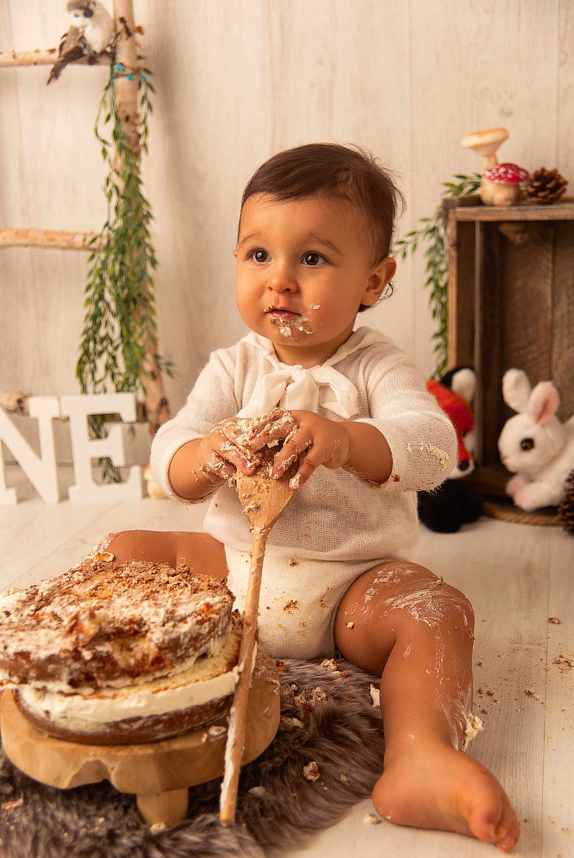 Noa participe au concours pour gagner de l'argent avec cette photo : baby, cake, messy, wooden_spoon, sitting, frosting, cute, indoor, plush_toy, decor, wooden_floor, greenery, child, face, hands, legs, smile, white_clothing, birthday, celebration