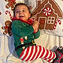 baby, blanket, child, christmas, clapping, cozy, festive, footwear, gingerbread_house, gingerbread_man, green_top, happy, holiday, indoors, infant, lying_down, pajamas, pillow, smiling, striped_pants