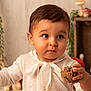 Noa participe au concours pour gagner de l'argent avec cette photo : toddler, child, pinecone, white_sweater, bow, indoor, portrait, cute, curious, soft_lighting, brown_hair, wood_background, greenery, natural, cozy, baby, sitting, closeup, person, warm_tones