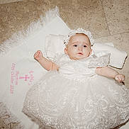 éabha is registered to the contest to win money with this photo: baby, infant, dress, white_dress, lace, headband, floor, tiled_floor, cloth, embroidery, baptism, celebration, cute, child, portrait, laying_down, indoors, person, newborn, ceremony