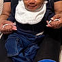 baby, child, infant, smile, dimples, bib, denim_pants, holding_hands, hair_puffs, adult, lap, indoor, black_clothing, blue_kneepads, socks, person, seated, cozy, cute, happy