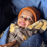 Zekani is registered to the contest to win money with this photo: baby, child, smile, face, beanie, hat, jacket, fuzzy_clothing, hand, carrier, blue, orange, cozy, warm, infant, portrait, cute, happy, indoor, person