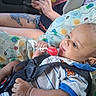 baby, infant, car_seat, lollipop, red_lollipop, vehicle, car_interior, adult, tattoo, hands, clothing, striped_shirt, blanket, patterned_fabric, seat_belt, portrait, close_up, sitting, alert, family