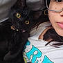 Navi is registered to the contest to win money with this photo: black_cat, cat, closeup, cozy, cute, earring, eyewear, face, feline, glasses, graphic_tee, human, indoor, person, pet, portrait, relaxed, snuggling, tshirt, yellow_eyes