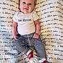 baby, infant, newborn, onesie, be_mine_text, striped_pants, red_socks, blanket, repeating_text_pattern, script_writing, blue_eyes, smiling, lying_down, portrait, close_up, cute, soft_texture, tiny_hand, tiny_feet, horizontal_stripes