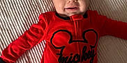 Kenneth is registered to the contest to win money with this photo: baby, infant, smiling_baby, red_onesie, mickey_print, blanket, bedding, ribbed_texture, lying_down, portrait, face, eyes, cheeks, hands, pajamas, cozy, cute, happy, nursery, soft_lighting