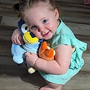 Ava is registered to the contest to win money with this photo: toddler, child, smiling, cute, pigtails, stuffed_animals, plush_toys, floor, barefoot, green_dress, indoor, happy, playful, cuddling, person, baby, blue_eyes, skin, young_child, squatting