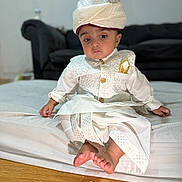 Hasnain is registered to the contest to win money with this photo: baby, barefoot, bed, child, couch, cute, floor, furniture, indoor, indoors, person, portrait, serious_expression, sitting, traditional_clothing, turban, white_outfit, wooden_floor, young, young_child