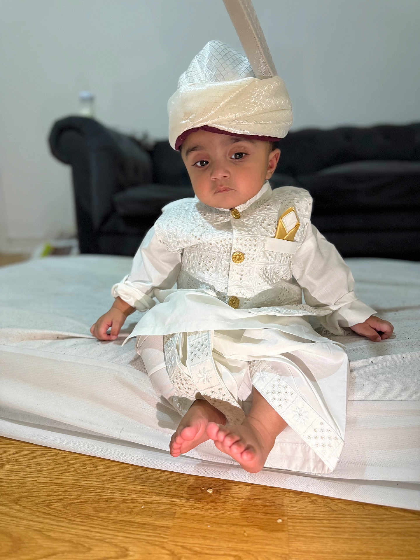 Hasnain is registered to the contest to win money with this photo: baby, barefoot, bed, child, couch, cute, floor, furniture, indoor, indoors, person, portrait, serious_expression, sitting, traditional_clothing, turban, white_outfit, wooden_floor, young, young_child
