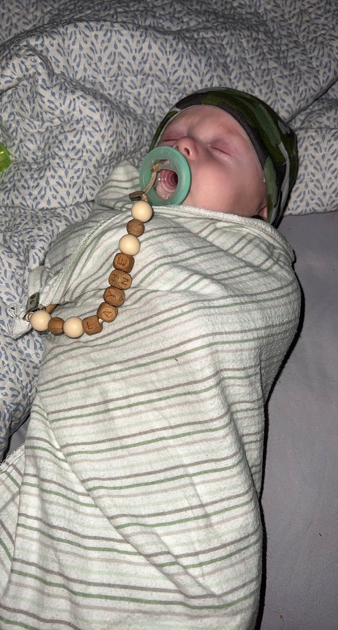 Layne is registered to the contest to win money with this photo: baby, baby_toddler_clothing, body_jewelry, cap, chain, chest, child, comfort, fashion_accessory, hand, headwear, human_body, jewellery, linens, military_camouflage, pattern, person, sleeve, toddler, wood