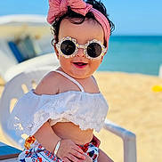 Jennah participe au concours pour gagner de l'argent avec cette photo : baby, child, sunglasses, headband, bow, beach, ocean, summer, white_clothing, floral_pattern, chair, smiling, happy, sitting, outdoor, sunny, cute, accessory, toddler, portrait