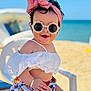 baby, child, sunglasses, headband, bow, beach, ocean, summer, white_clothing, floral_pattern, chair, smiling, happy, sitting, outdoor, sunny, cute, accessory, toddler, portrait