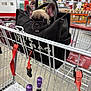 puppy, dog, french_bulldog, shopping_cart, bag, black_bag, warehouse, bottle, purple_caps, concrete_floor, person_blurred, orange_shelves, retail_store, pet, curious, cute, animal, indoor, shopping, container