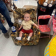 Gunner joined the competition — help win amazing prizes! baby, child, armchair, camo_pattern, toy_horse, pink_chair, floor, person, socks, shorts, tshirt, indoor, plastic_cup, adult, toys, retail_store, curious_expression, seated, carpet, floor_tiles