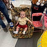 baby, child, armchair, camo_pattern, toy_horse, pink_chair, floor, person, socks, shorts, tshirt, indoor, plastic_cup, adult, toys, retail_store, curious_expression, seated, carpet, floor_tiles