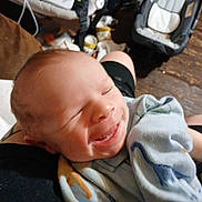 Jacob is registered to the contest to win money with this photo: baby, smiling, blanket, dinosaur_print, infant, person, arms, indoor, wooden_floor, baby_gear, comfort, cozy, closeup, face, head, newborn, holding, child, cute, happy