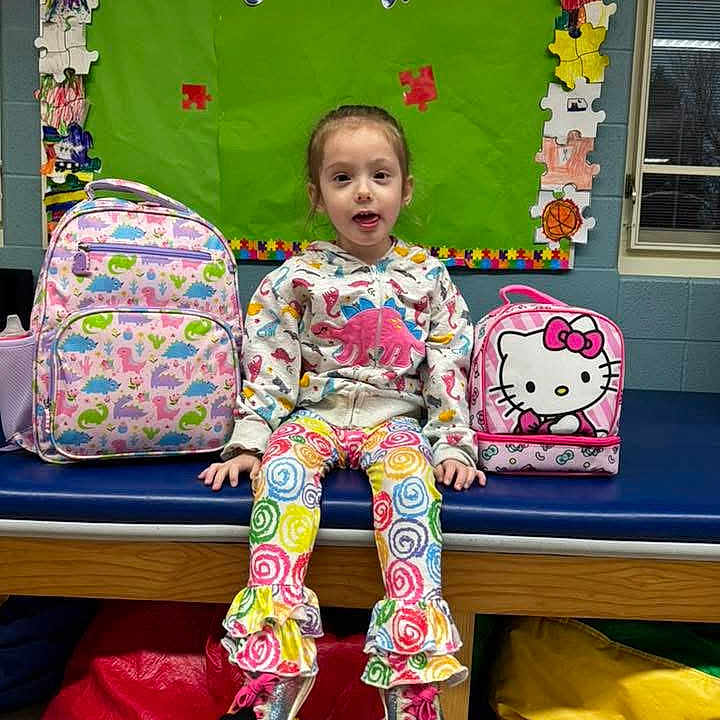 Brooklyn is registered to the contest to win money with this photo: child, girl, school, classroom, backpack, pink_backpack, hello_kitty, colorful_clothing, rainbow_pants, sparkly_shoes, sitting, smiling, portrait, indoors, bulletin_board, puzzle_pieces, window, bench, school_supplies, colorful