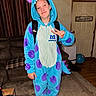 backpack, balloon, blue, child, costume, couch, door, hood, horns, indoors, living_room, monster_costume, onesie, peace_sign, portrait, purple, rug, smiling, sneakers, young_person