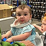 Tallulah joined the competition — help win amazing prizes! baby, child, shopping_cart, store, jewelry, accessories, bib, expression, curly_hair, red_hair, sleeveless_outfit, hand, person, retail, shelf, box, curiosity, indoor, parent, candid