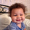 Giovanni is registered to the contest to win money with this photo: baby, bed, bedding, bedroom, blanket, blue_outfit, child, closeup, curly_hair, face, happy, headboard, home, indoor, infant, pillow, portrait, sitting, smiling, wallpaper