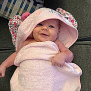 Sutton is registered to the contest to win money with this photo: baby, smiling, towel, pink, hood, floral, ears, couch, cushion, pattern, infant, wrapped, soft, comfortable, happy, child, portrait, indoor, cute, face