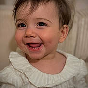 Sylena participe au concours pour gagner de l'argent avec cette photo : baby, child, infant, portrait, close_up, smiling, teeth, tongue, eyes, eyelashes, hair, ear, white_clothing, ruffled_collar, rosy_cheeks, skin, happy, indoor, soft_lighting, candid