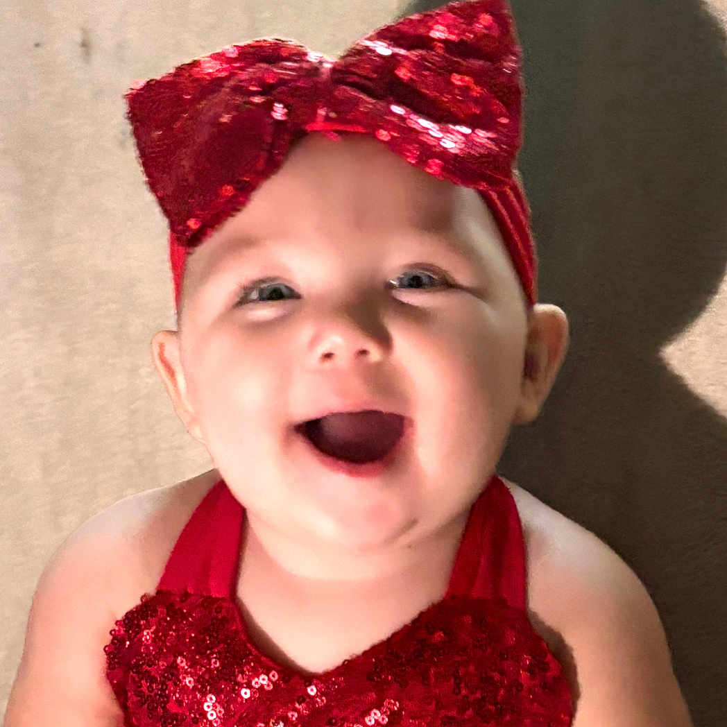 Khloe joined the competition — help win amazing prizes! apparel, baby, cheerful, child, cute, face, happy, headband, headwear, indoor, infant, joyful, person, portrait, red_bow, red_clothing, sequins, skin, smiling, young_child