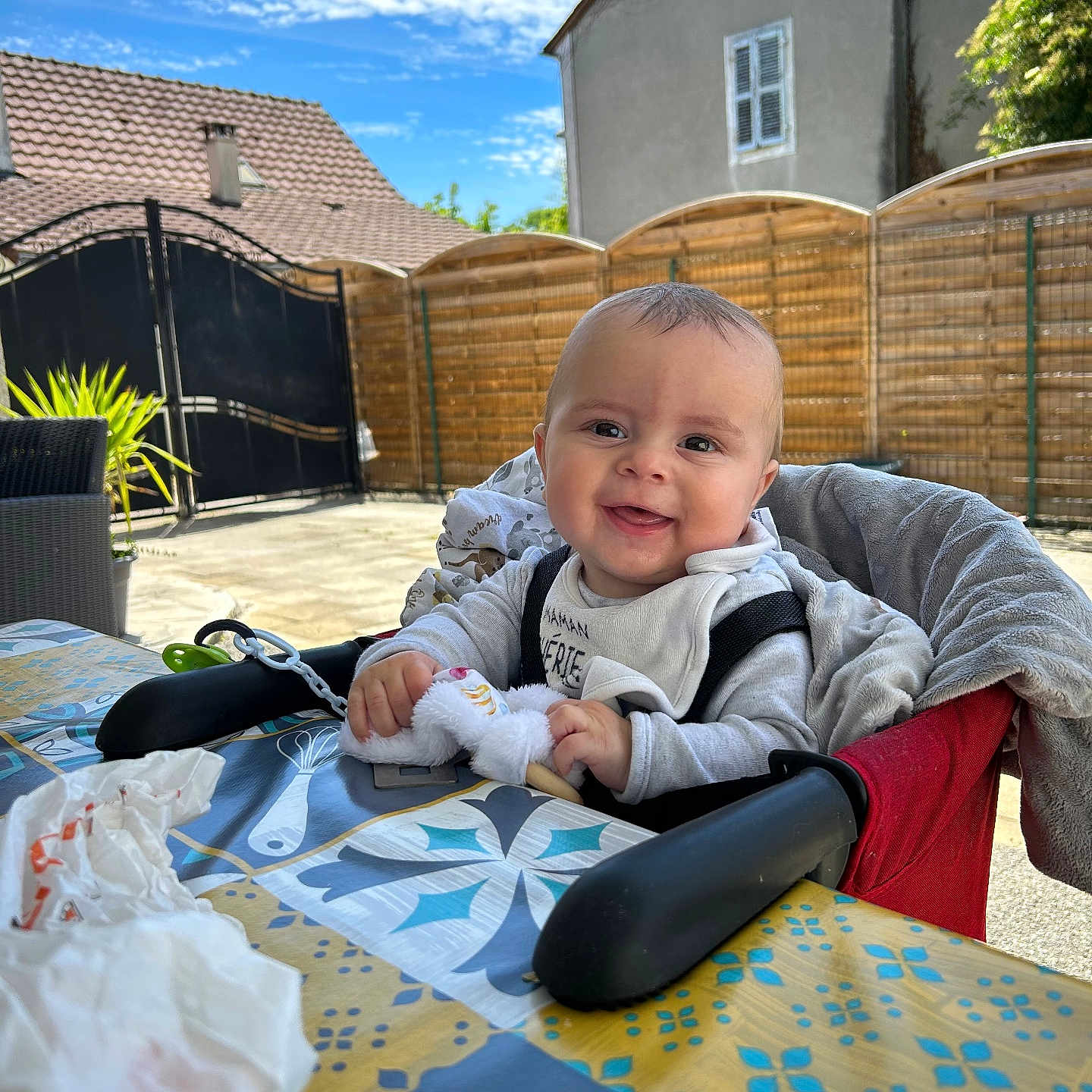 Noah a rejoint le concours — aidez-le/la à gagner de superbes lots ! baby, backyard, child, clothing, clouds, daylight, face, fence, happy, high_chair, house, outdoor, patterned_tablecloth, person, plant, seat, sky, smile, table, toy