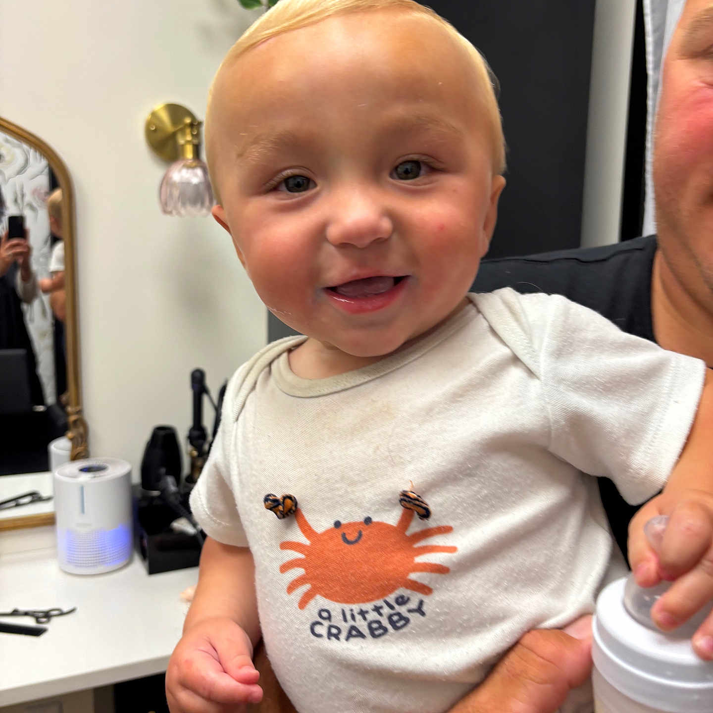 Bobby joined the competition — help win amazing prizes! baby, child, infant, smile, face, person, white_shirt, cartoon_crab, bottle, hand, indoor, mirror, plant, grooming_tools, adult_arm, cute, happy, closeup, holding, milk